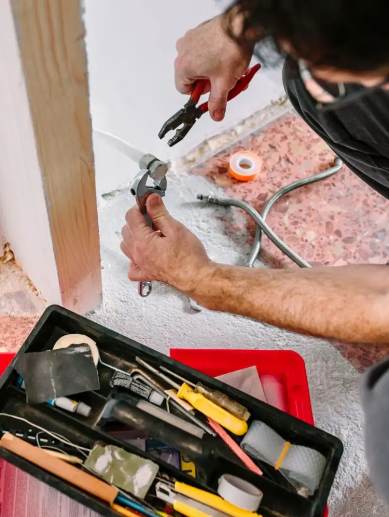 Plumber repairing pipe fittings with wrench and pliers for NES home plumbing FAQ.